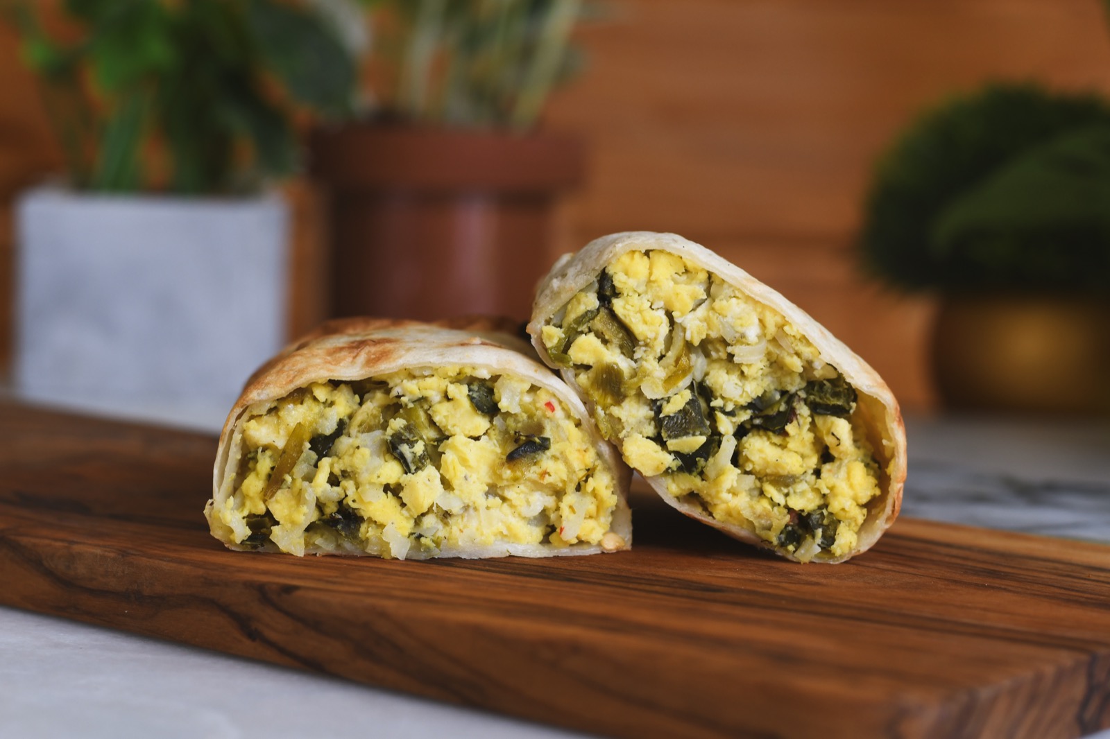 Two green chile breakfast burritos cut open on a wooden board